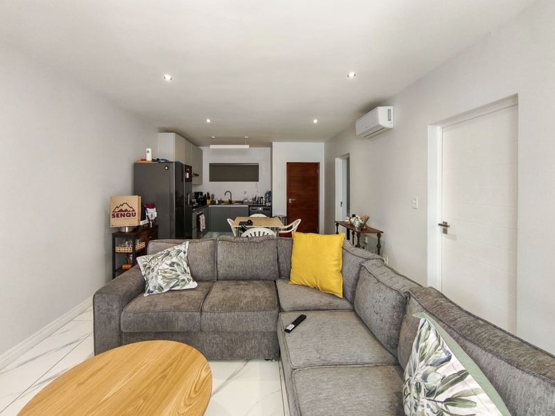 An open-plan living and kitchen area featuring modern tiled flooring, recessed lighting, and a wall-mounted air conditioning unit.