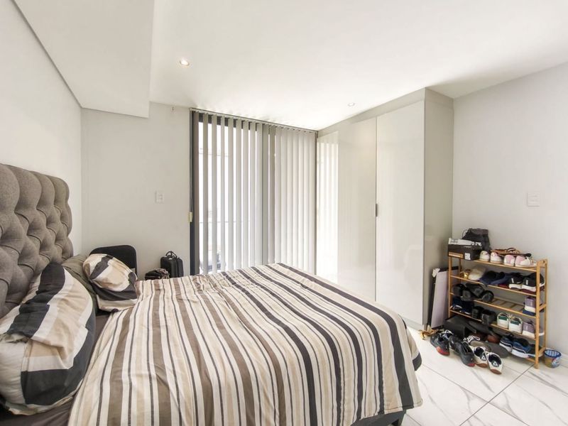 A modern bedroom featuring built-in cupboards, tiled flooring, and vertical blinds, offering a clean and functional living space.