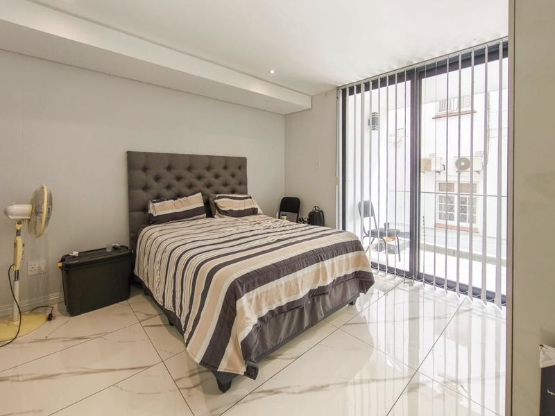 A bright bedroom featuring large format tiled flooring, recessed ceiling lighting, and a sliding glass door providing access to a private balcony.