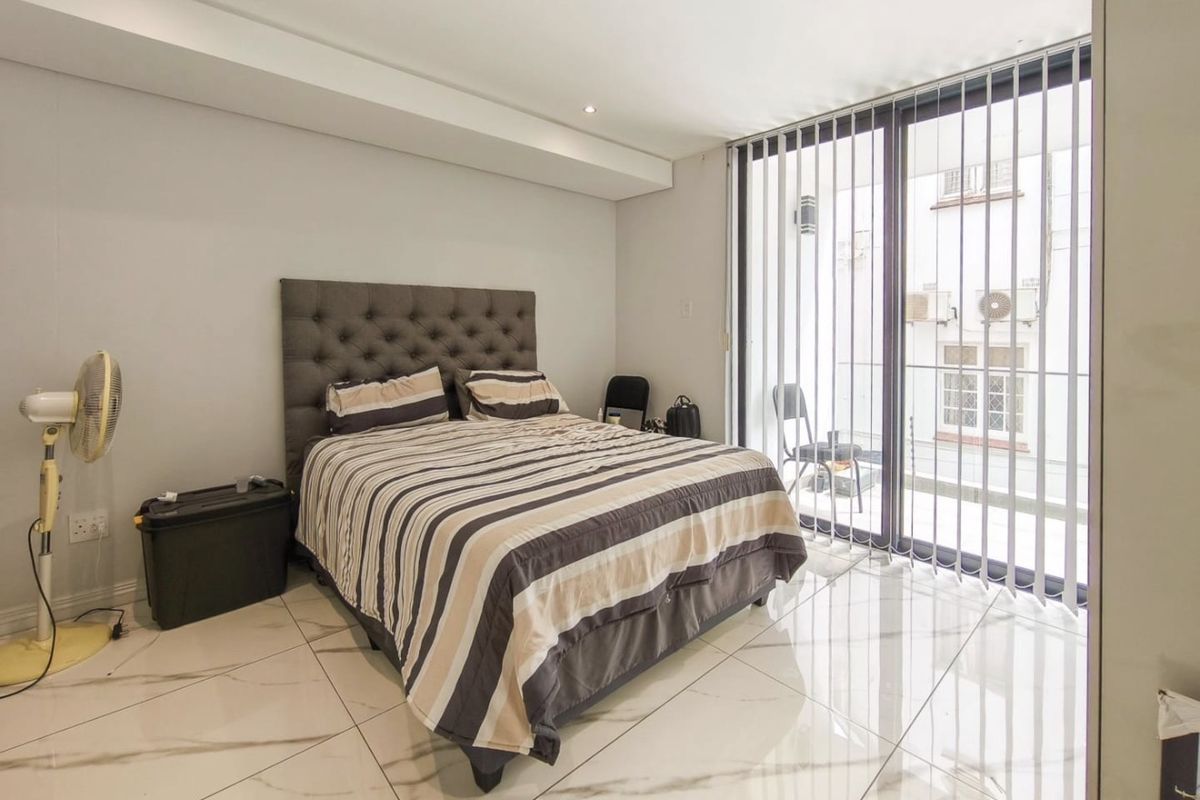 A bright bedroom featuring large format tiled flooring, recessed ceiling lighting, and a sliding glass door providing access to a private balcony.