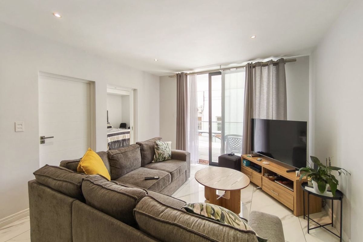 A bright, modern living room featuring polished tiled floors, recessed lighting, and direct access to a balcony through a large sliding glass door.