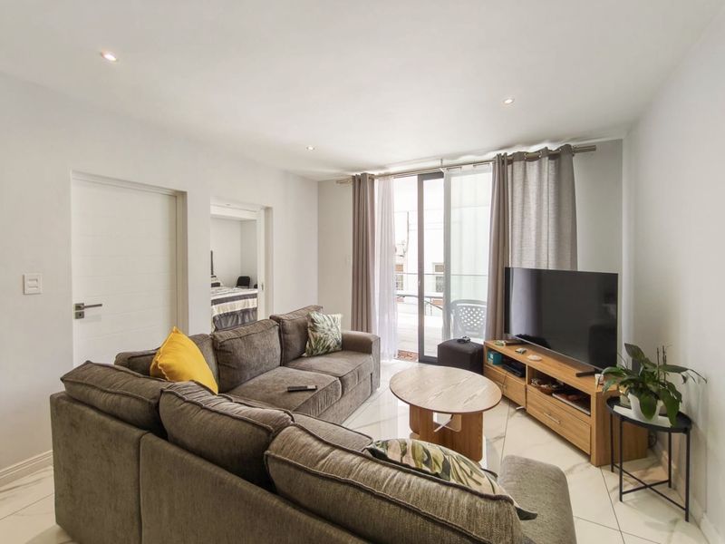 A bright, modern living room featuring polished tiled floors, recessed lighting, and direct access to a balcony through a large sliding glass door.