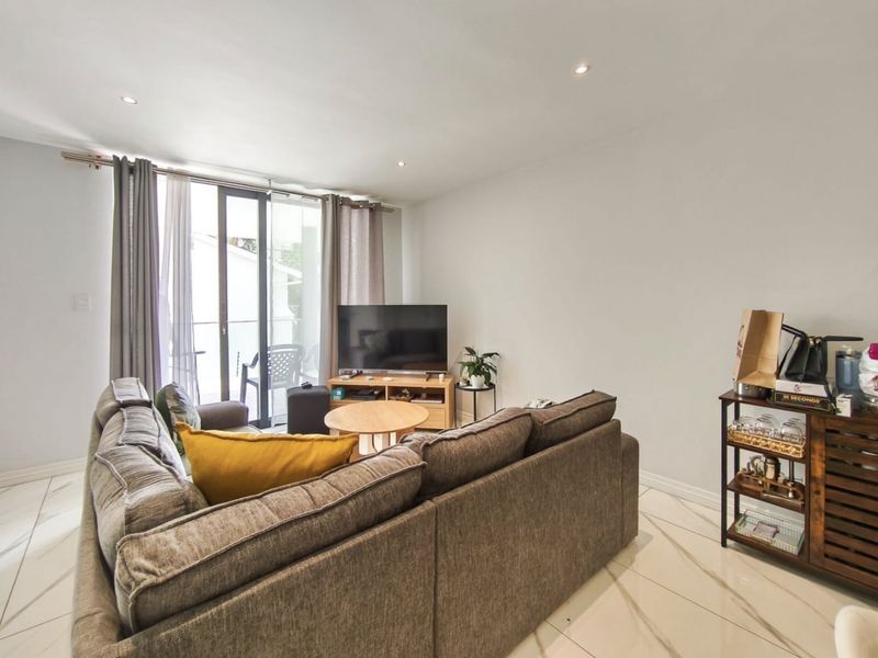 A bright living room featuring large format tiled flooring, recessed downlighting, and a sliding glass door providing access to an outdoor balcony area.