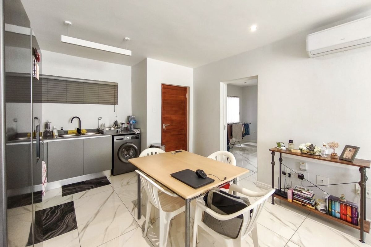 Open-plan living and kitchen area featuring modern marble-look floor tiles, sleek cabinetry, integrated laundry facilities, and a wall-mounted air conditioning unit.