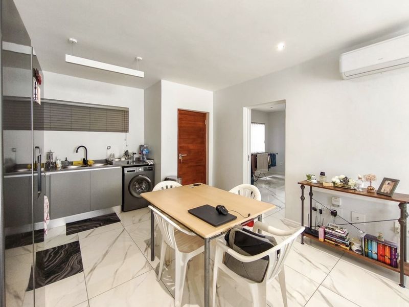 Open-plan living and kitchen area featuring modern marble-look floor tiles, sleek cabinetry, integrated laundry facilities, and a wall-mounted air conditioning unit.