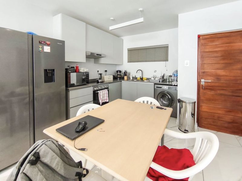 Open-plan kitchen area featuring modern grey cabinetry, integrated appliances, tiled flooring, and a functional layout adjacent to a wooden entrance door.