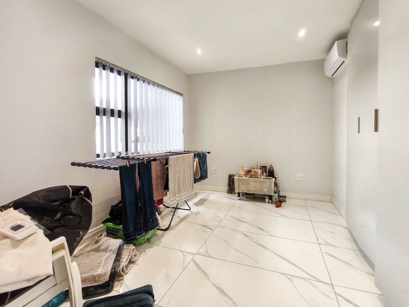 A bright bedroom featuring large format marble-look floor tiles, built-in storage, vertical blinds, and a wall-mounted air conditioning unit.