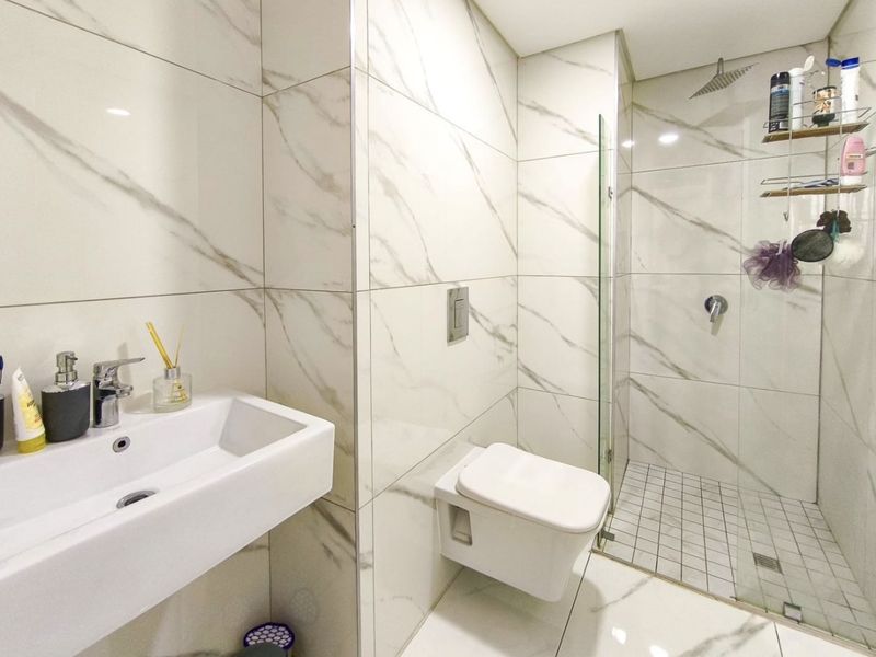 Modern bathroom featuring marble-look wall tiles, a wall-mounted basin, a concealed cistern toilet, and a walk-in shower with a glass screen.