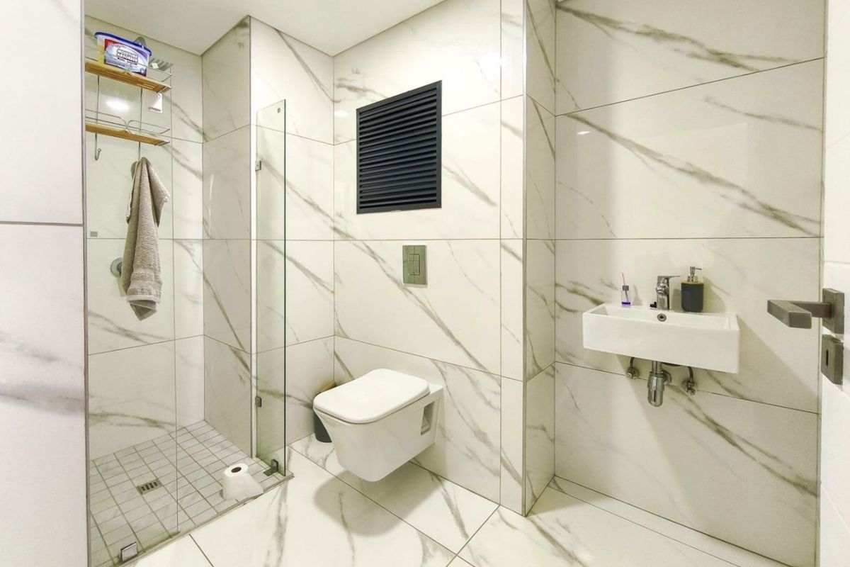 Modern bathroom featuring marble-look wall and floor tiles, a wall-mounted toilet with concealed cistern, and a glass-enclosed shower area.