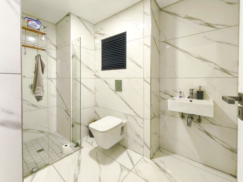 Modern bathroom featuring marble-look wall and floor tiles, a wall-mounted toilet with concealed cistern, and a glass-enclosed shower area.