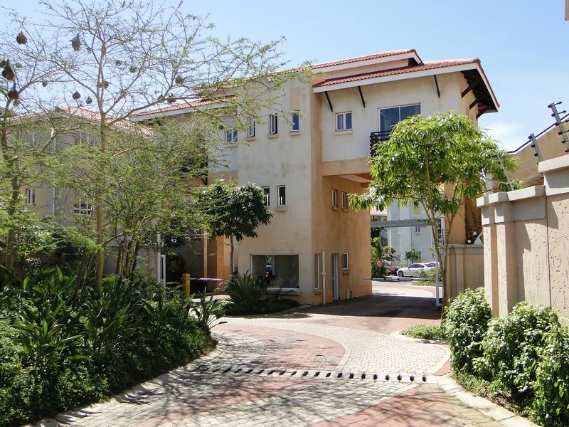 The entrance to the apartment complex features a paved driveway, security gate, and perimeter wall with electric fencing.