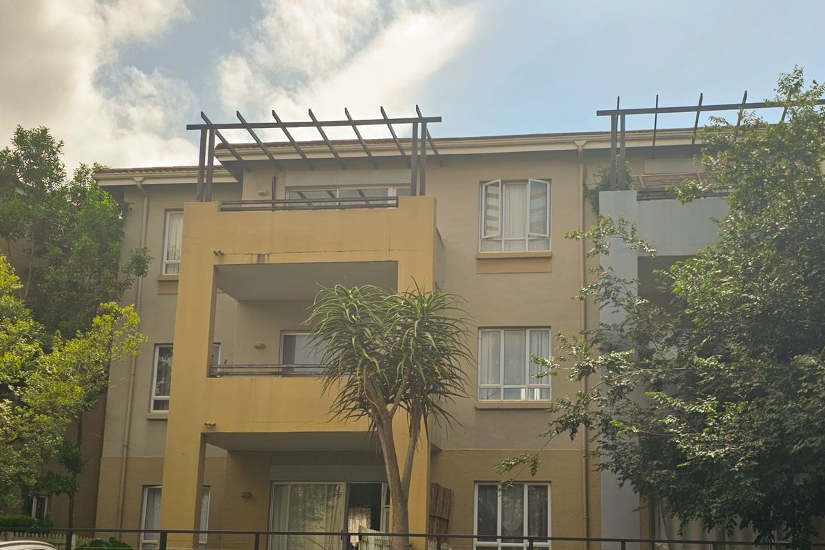 Exterior view of an apartment building featuring private balconies with pergolas and large sliding glass doors.