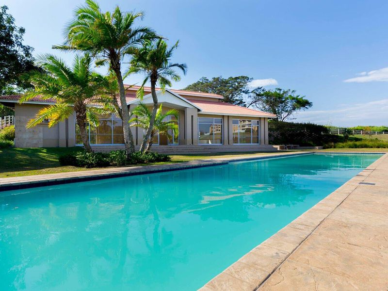A spacious swimming pool set in a landscaped garden, featuring a tiled surround and a view of the main building's rear facade.