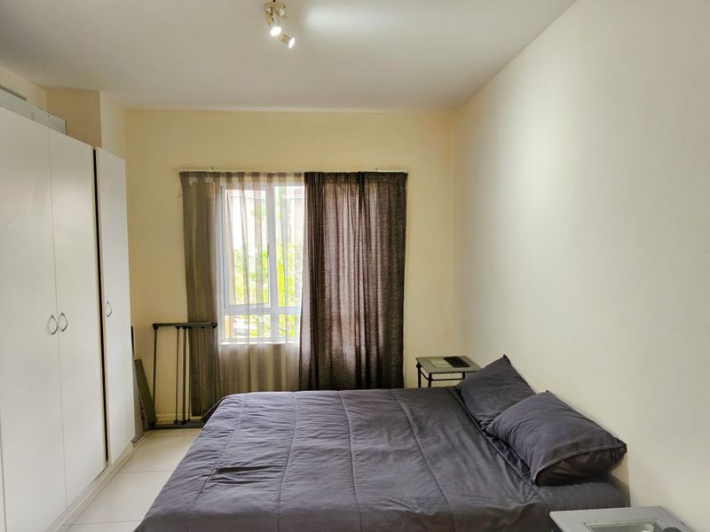 A functional bedroom featuring tiled flooring, a built-in wardrobe, and a window allowing natural light.