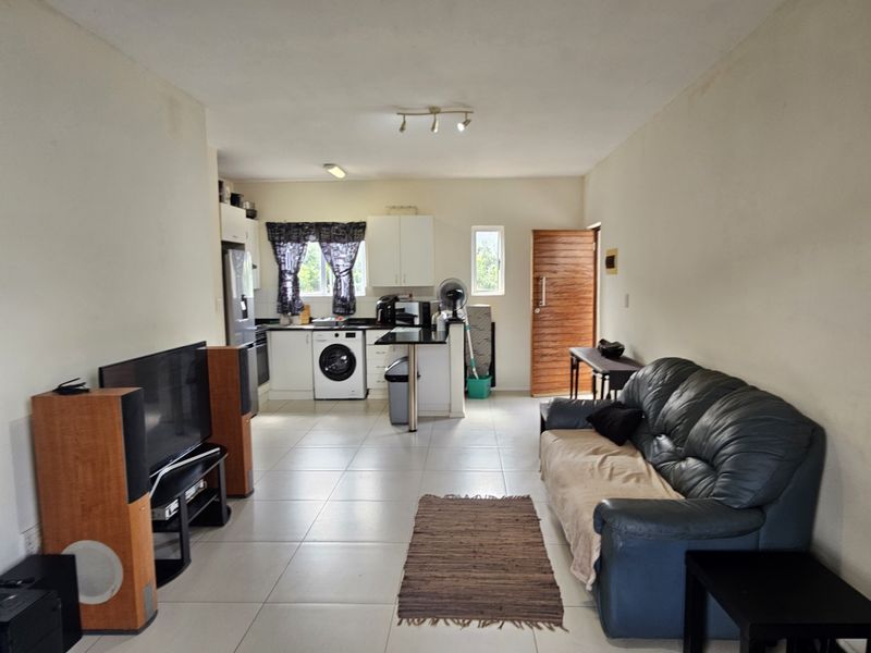 Open-plan living area featuring a functional kitchen with breakfast bar, tiled flooring, and direct access to the main entrance.