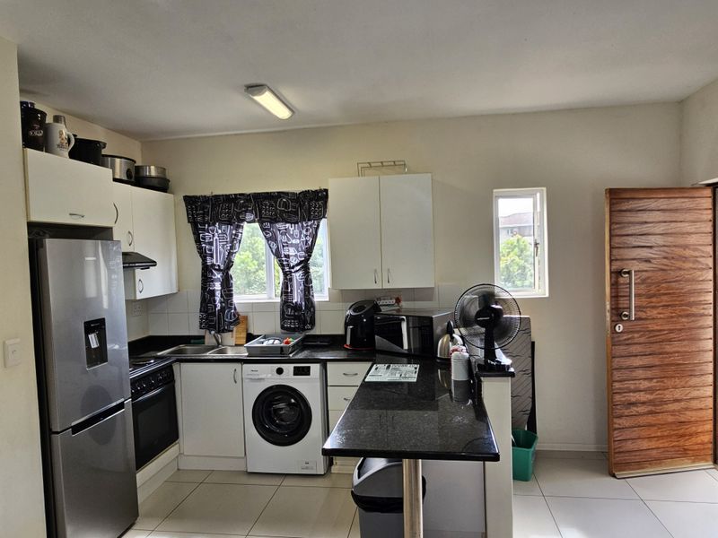 Functional kitchen featuring granite countertops, built-in cabinetry, integrated oven and hob, tiled backsplash, and direct access to the main entrance.