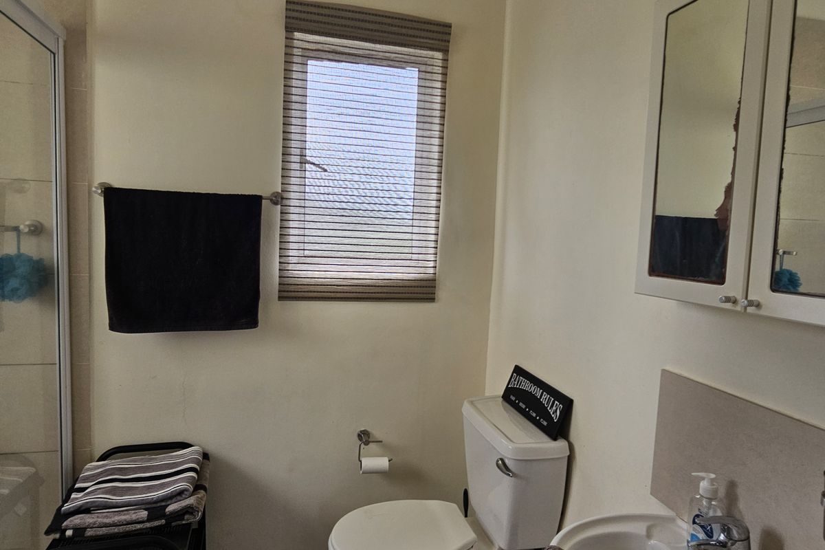 A functional bathroom featuring a shower enclosure, pedestal basin, and wall-mounted medicine cabinet, providing essential amenities in a compact layout.