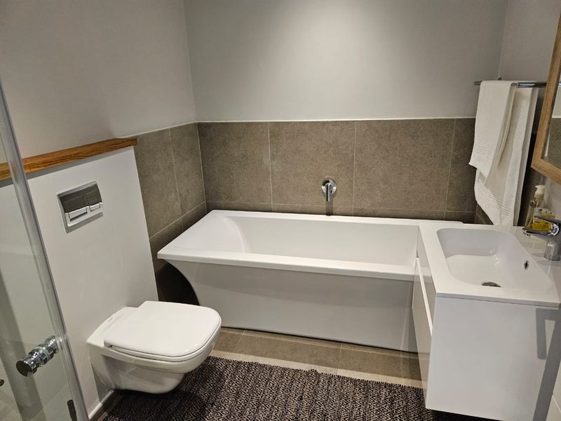 Modern bathroom featuring a wall-hung toilet with concealed cistern, a sleek freestanding bathtub, and a contemporary vanity basin with wall-mounted fixtures.