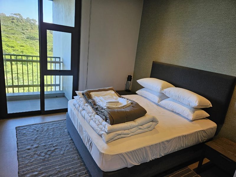 A well-maintained bedroom featuring textured wallpaper, tiled flooring, and a large sliding glass door providing direct access to a private balcony with scenic views.