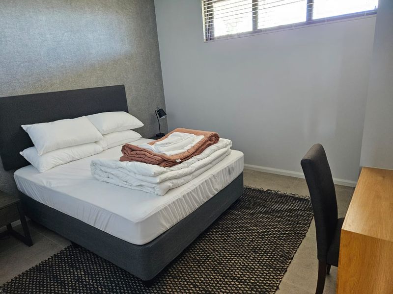 A well-lit bedroom featuring a textured accent wall, neutral flooring, and horizontal window blinds.