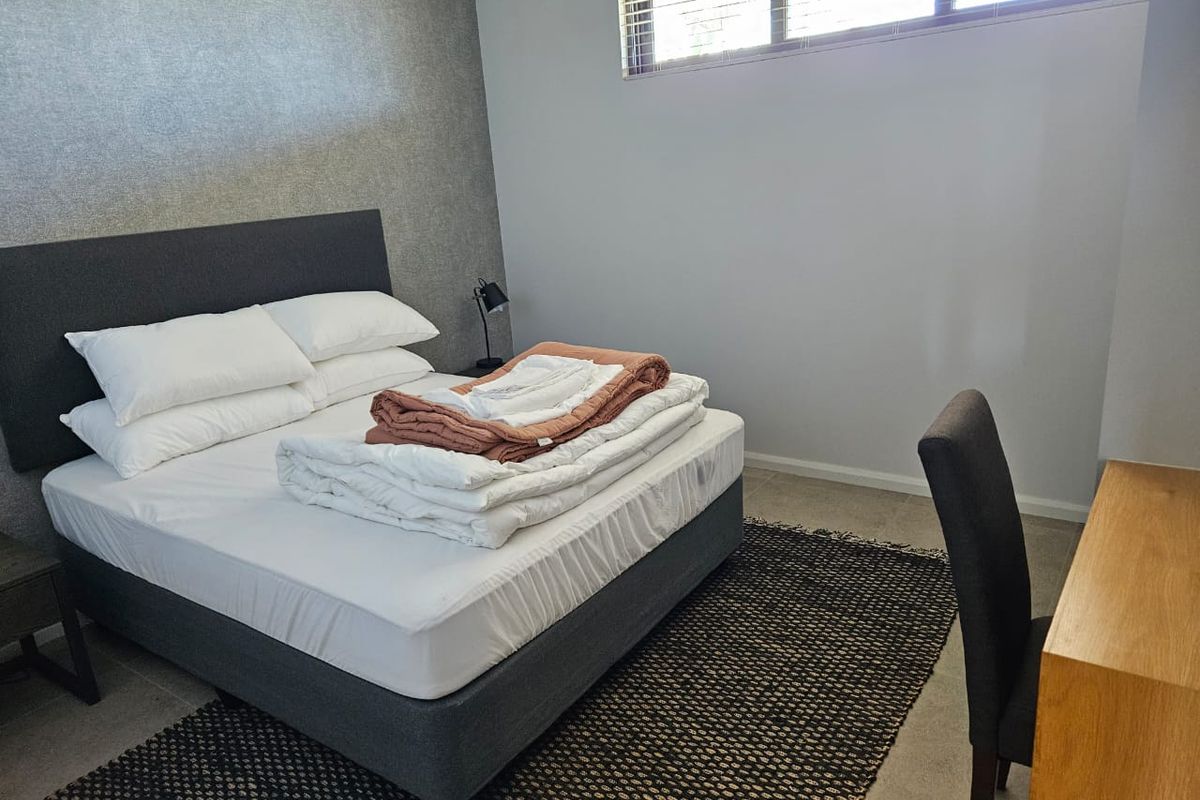 A well-lit bedroom featuring a textured accent wall, neutral flooring, and horizontal window blinds.
