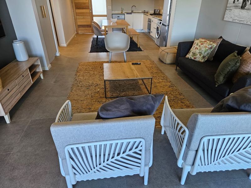An open-plan living and kitchen area featuring modern tiled flooring, neutral cabinetry, and integrated kitchen appliances in a well-maintained apartment setting.