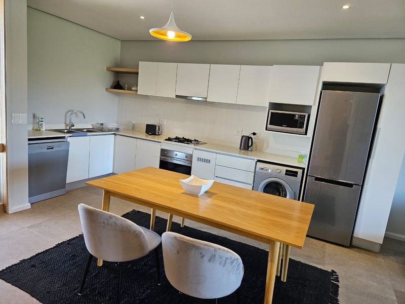 Modern open-plan kitchen featuring sleek white cabinetry, integrated appliances, gas hob, and tiled flooring, seamlessly flowing into the dining area.