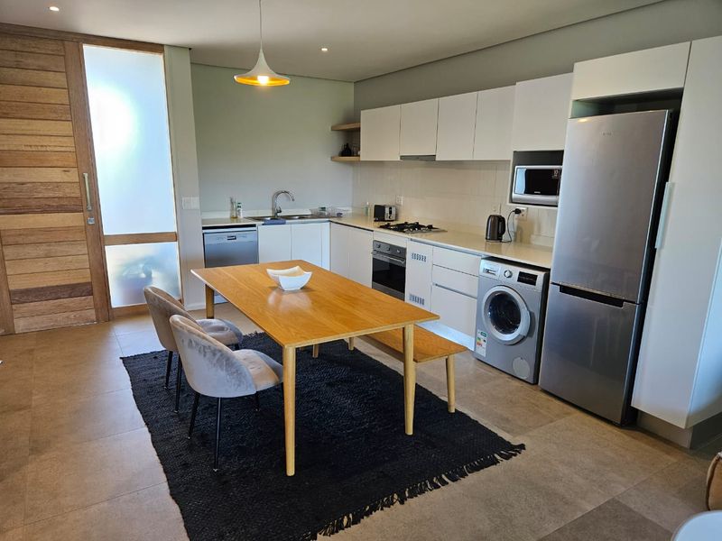 Modern open-plan kitchen featuring sleek white cabinetry, stone countertops, integrated appliances, and tiled flooring, seamlessly connected to a dining area.