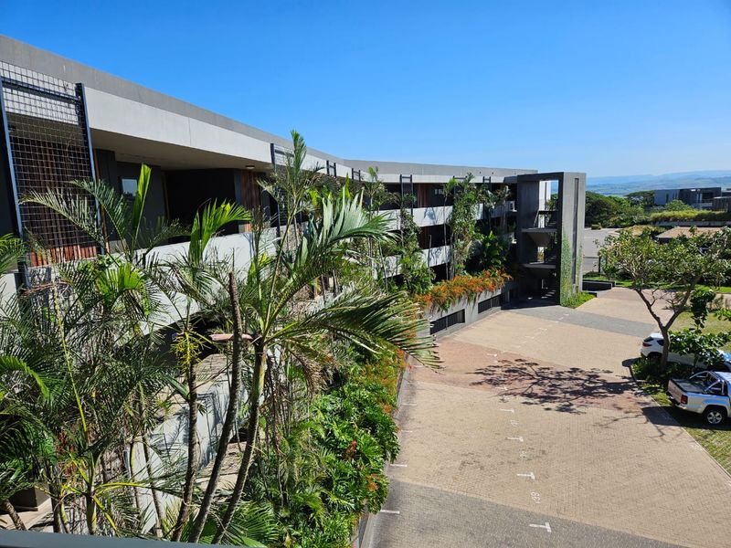 Elevated view of a modern apartment complex featuring contemporary concrete architecture, integrated vertical gardens, and a paved parking area.