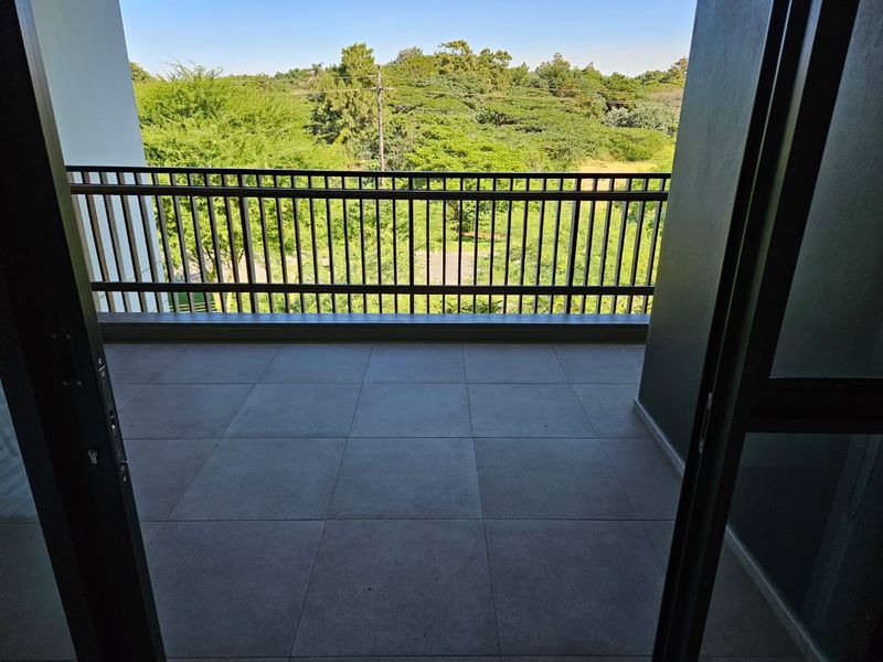 A clean, modern balcony featuring tiled flooring and a secure metal balustrade, offering pleasant views of the surrounding greenery.