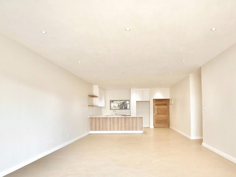 A bright, modern open-plan living and kitchen area featuring neutral finishes, recessed lighting, and a functional kitchen island with integrated cabinetry.