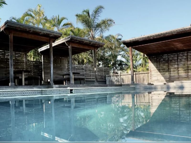 Outdoor pool area featuring multiple timber gazebos and privacy screening, providing a shaded communal space for residents.