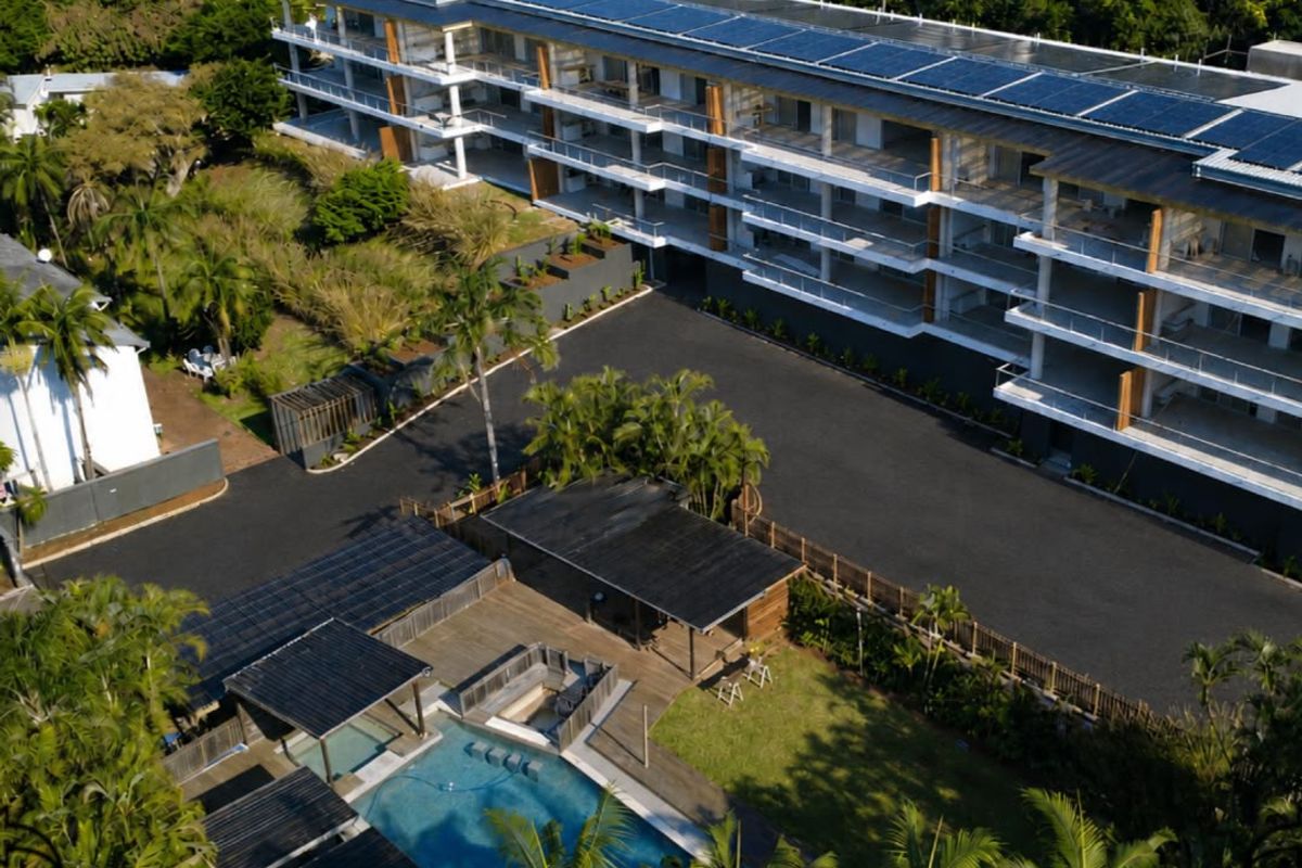 Aerial view of a modern apartment complex featuring solar panels, a swimming pool with timber decking, and landscaped grounds.
