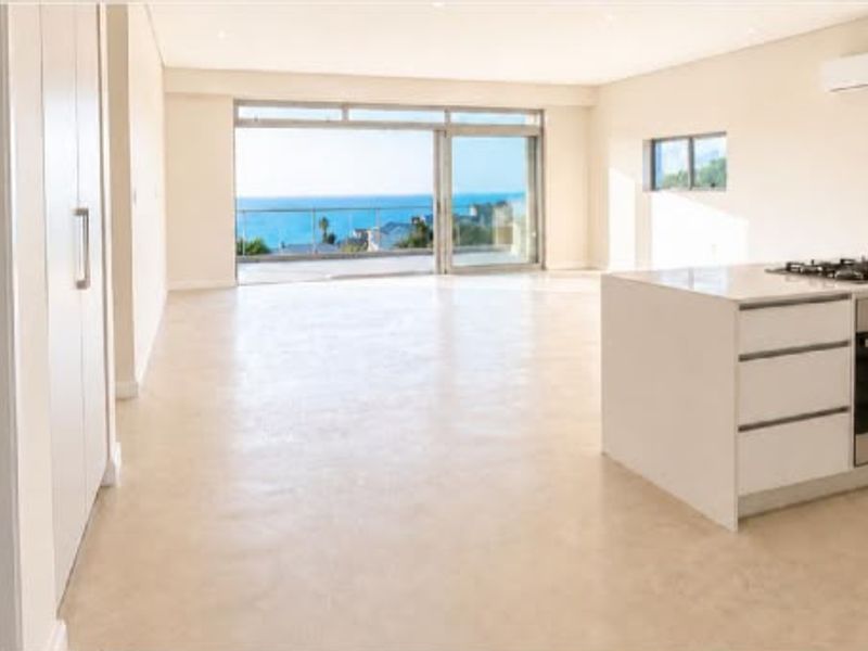 Spacious open-plan living area featuring a modern kitchen island, built-in appliances, and large sliding doors opening to a scenic coastal view.