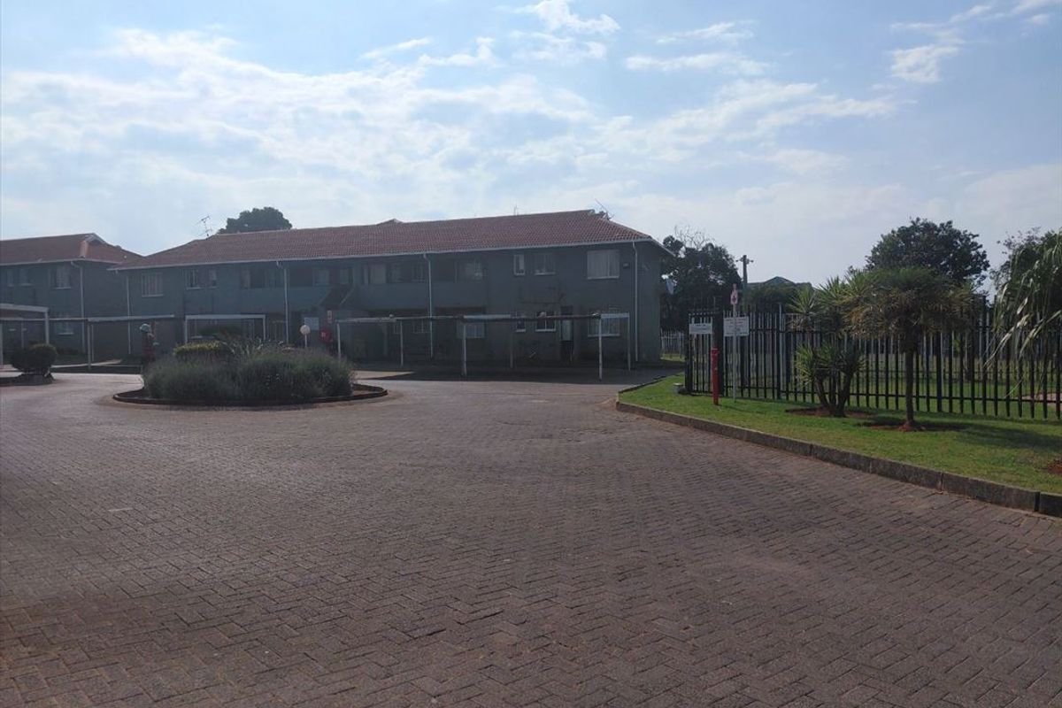 Exterior view of a townhouse complex featuring a paved driveway, covered carports, and secure perimeter fencing.