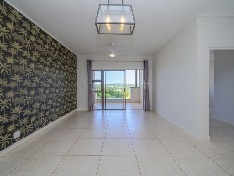 Spacious open-plan living area featuring neutral tiled flooring, a modern ceiling fan, feature wallpaper, and direct access to a private balcony.