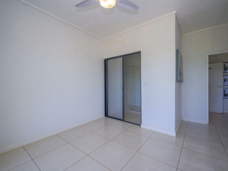 A bright, empty bedroom featuring neutral tiled flooring, a ceiling fan, and built-in sliding mirror wardrobe doors.