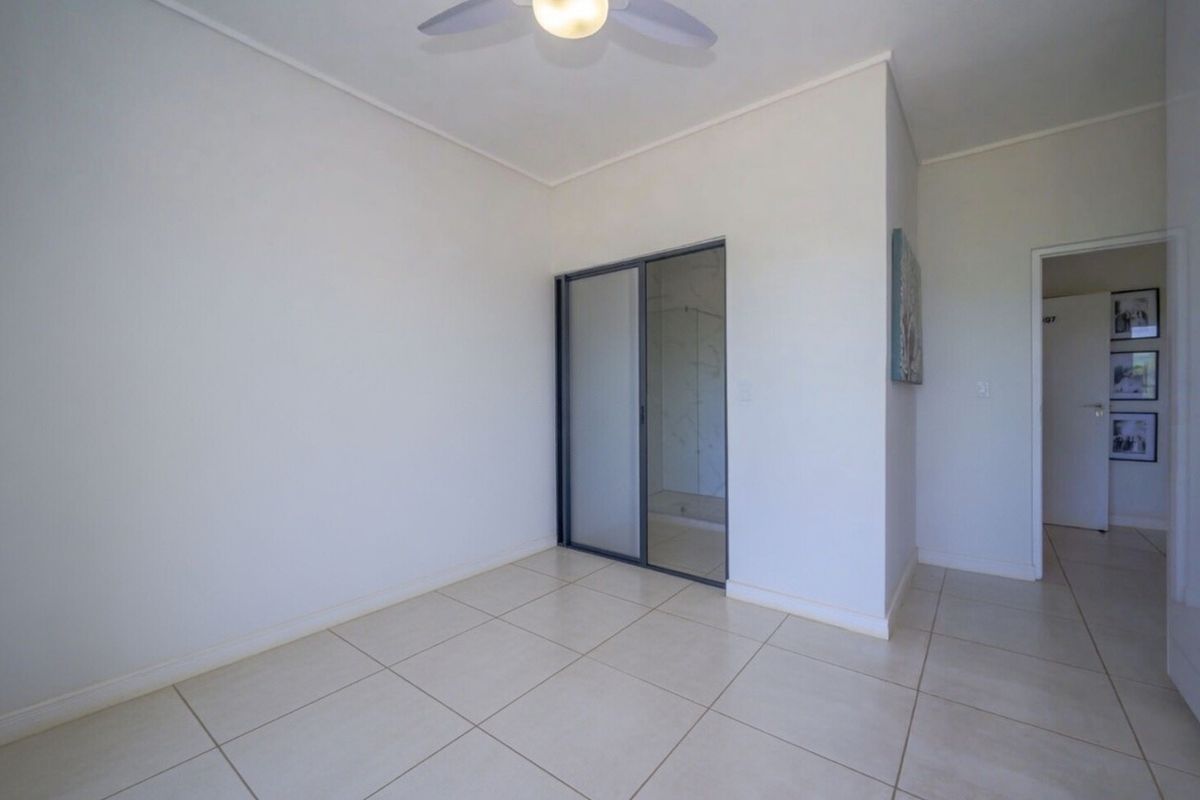 A bright, empty bedroom featuring neutral tiled flooring, a ceiling fan, and built-in sliding mirror wardrobe doors.