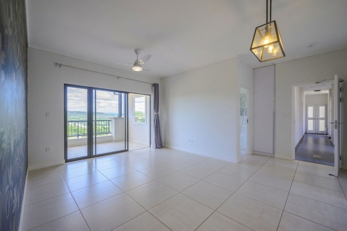 Spacious, light-filled living area featuring neutral tiled flooring, a ceiling fan, and large sliding doors opening onto a balcony with scenic views.