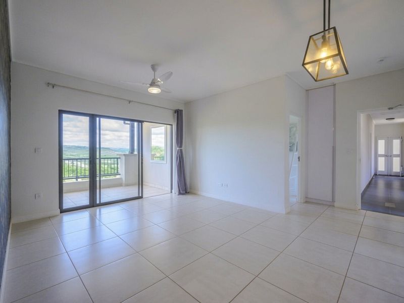 Spacious, light-filled living area featuring neutral tiled flooring, a ceiling fan, and large sliding doors opening onto a balcony with scenic views.