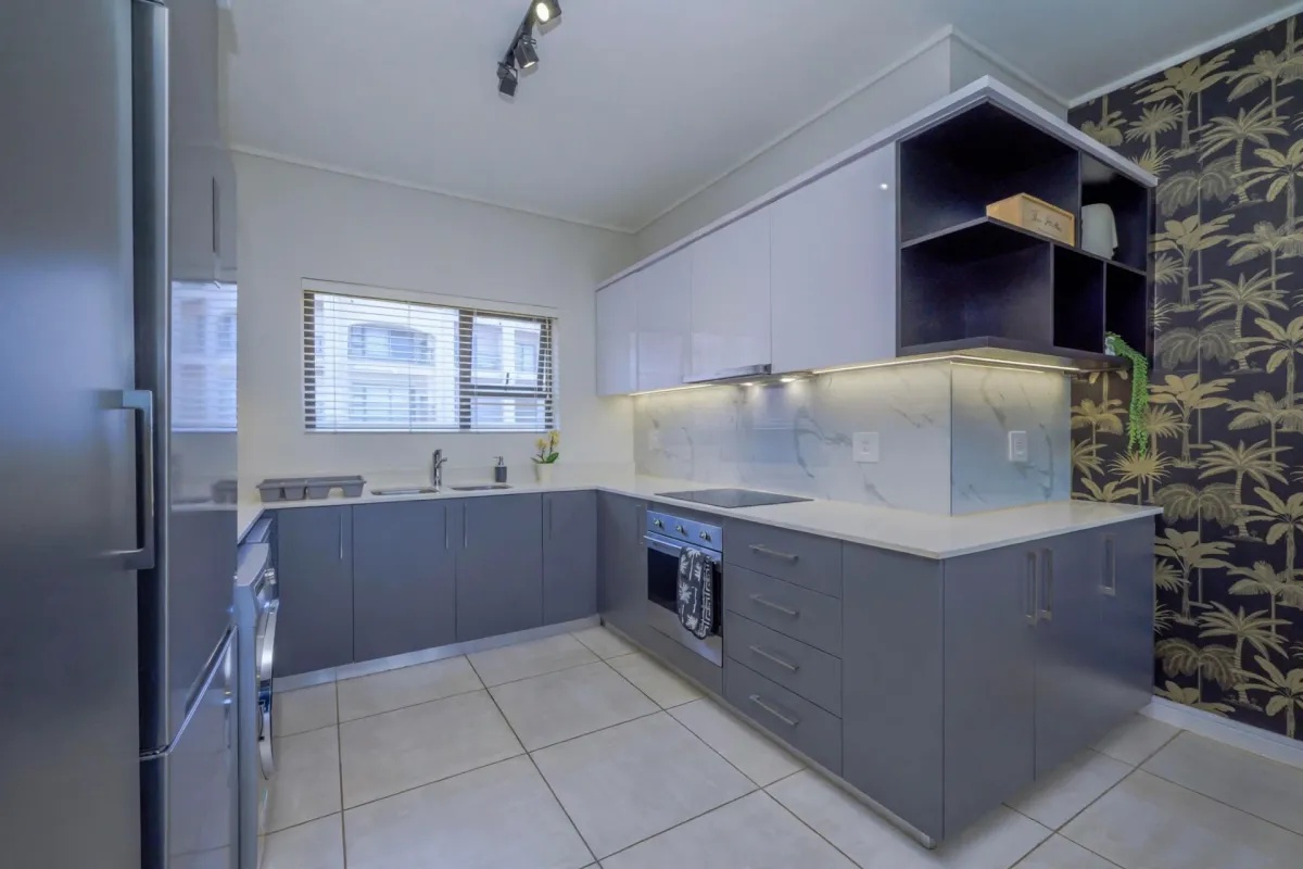 Modern kitchen featuring sleek grey cabinetry, stone countertops, integrated appliances, and stylish patterned wallpaper, offering a clean and contemporary culinary space.
