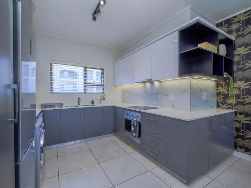 Modern kitchen featuring sleek grey cabinetry, stone countertops, integrated appliances, and stylish patterned wallpaper, offering a clean and contemporary culinary space.