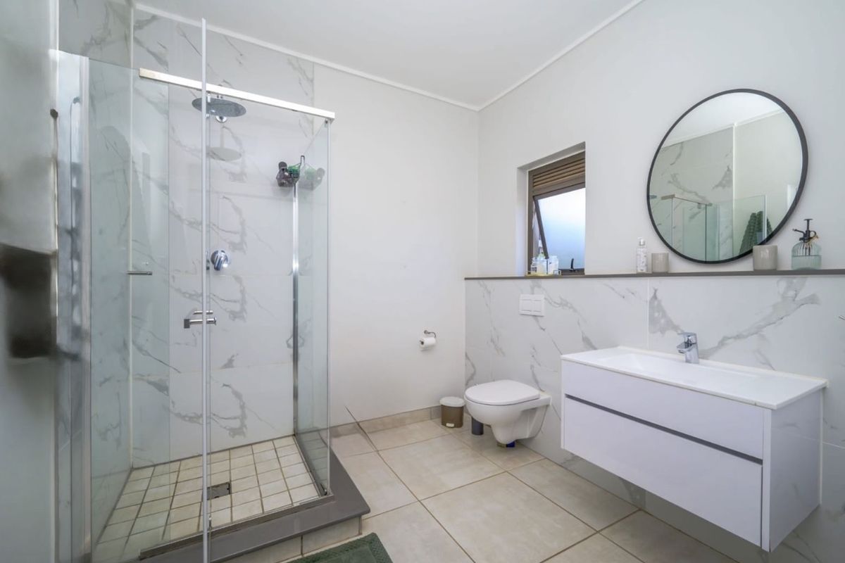 Modern bathroom featuring a glass-enclosed shower, wall-mounted toilet, and a sleek floating vanity with marble-look wall tiling.