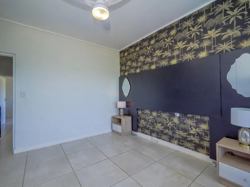 A bedroom featuring tiled flooring, a ceiling fan, and a decorative feature wall with a built-in headboard panel.