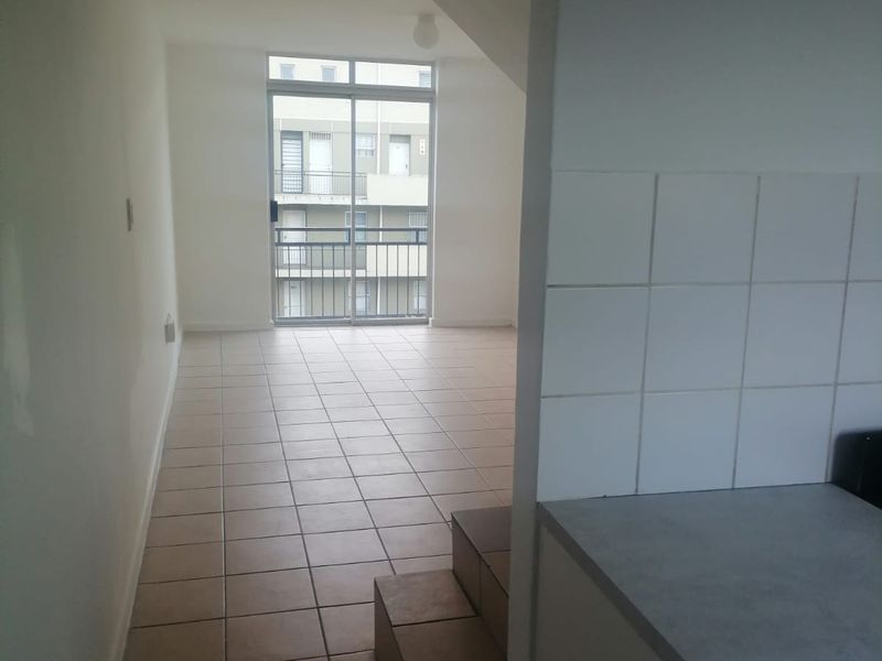 An open-plan living area featuring tiled flooring, a staircase, and a sliding glass door leading to a balcony, with an adjacent kitchen area.