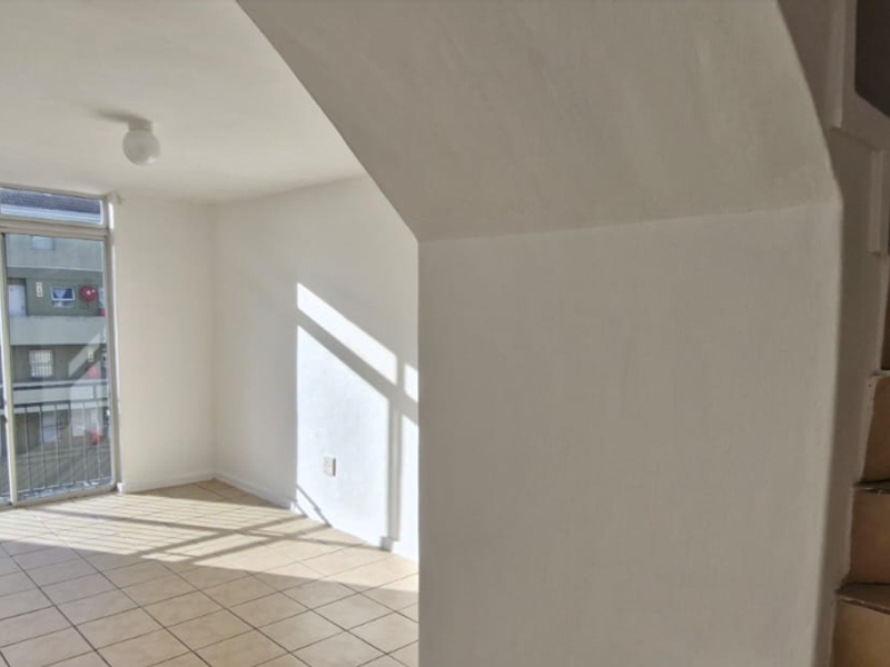 An empty living area featuring tiled flooring, a sliding glass door leading to a balcony, and an adjacent staircase with ceramic tiling.