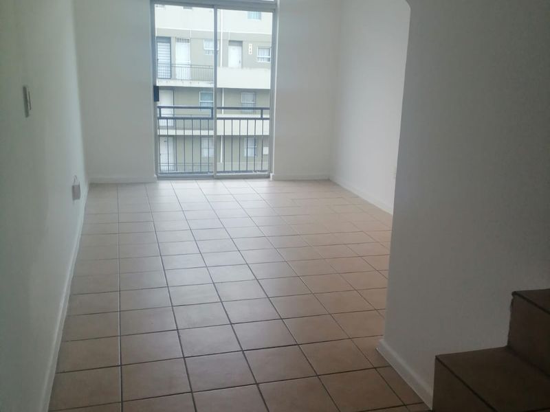 An empty, open-plan living area featuring neutral tiled flooring and a sliding glass door leading to a balcony, with an adjacent staircase.