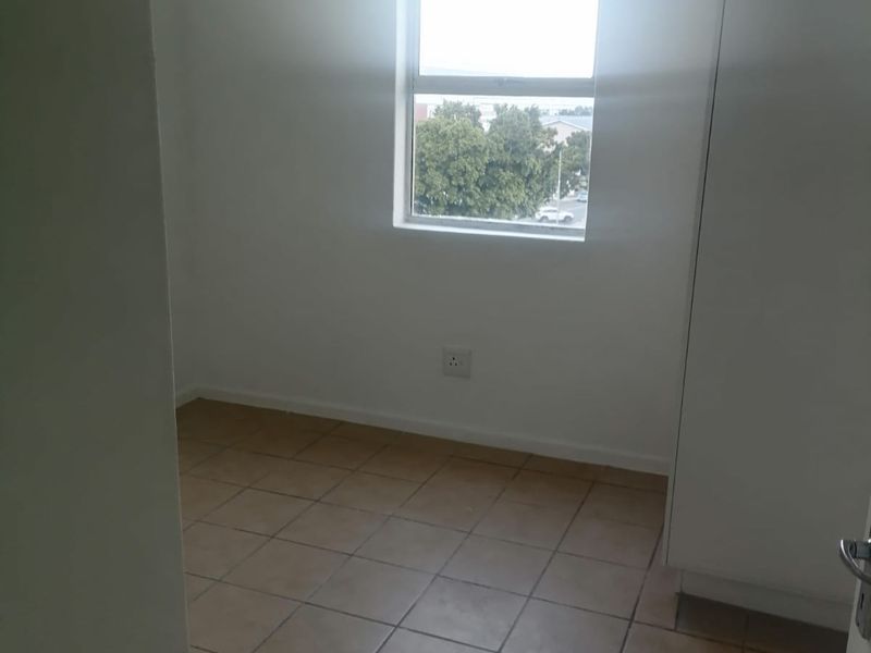 An empty bedroom featuring tiled flooring, a built-in cupboard, and a window providing natural light.