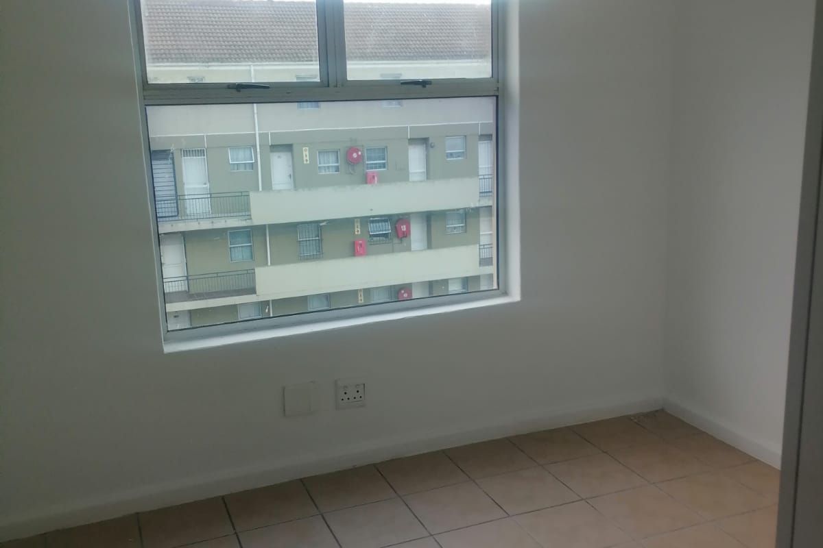 An empty bedroom featuring tiled flooring and a large window with views of the surrounding apartment complex.