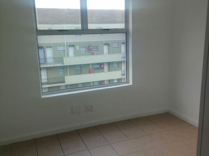 An empty bedroom featuring tiled flooring and a large window with views of the surrounding apartment complex.